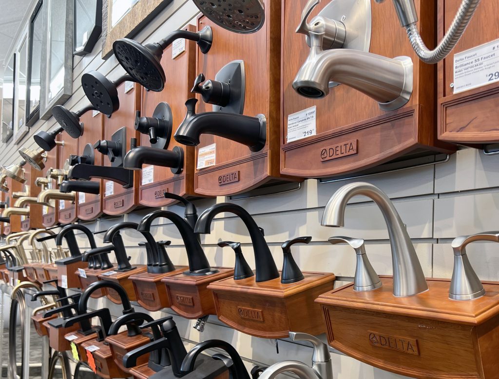 Lavatory faucets and shower heads at the Sioux Falls showroom in brushed nickel, matte black, and brushed gold finishes on wall displays.